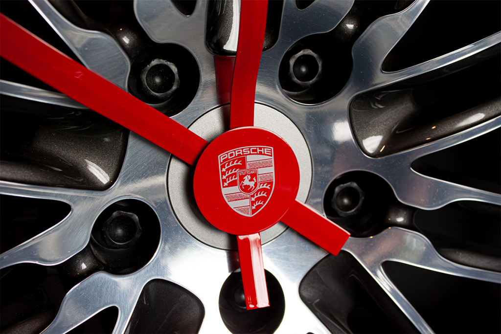 Nahaufnahme einer Porsche-Felge, die von roten Uhrzeigern durchzogen ist und so als exklusive Wanduhr gestaltet wurde, umgesetzt von Präsentstudio Soennecken als individuelles Werbemittel