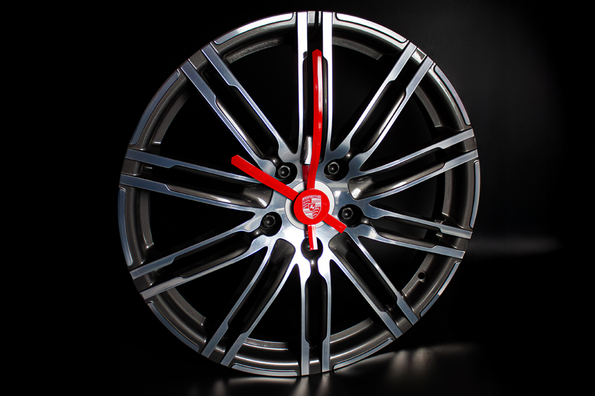 Exklusive Wanduhr aus einer Porsche-Felge mit roten Uhrzeigern auf schwarzem Hintergrund, umgesetzt von Präsentstudio Soennecken als individuelles Werbemittel